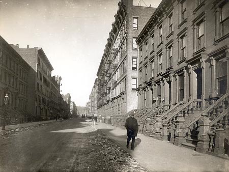 A quiet Harlem street shows tall brownstones and a few pedestrians, reflecting Philip A. Payton Jr.s impact on the neighborhood.