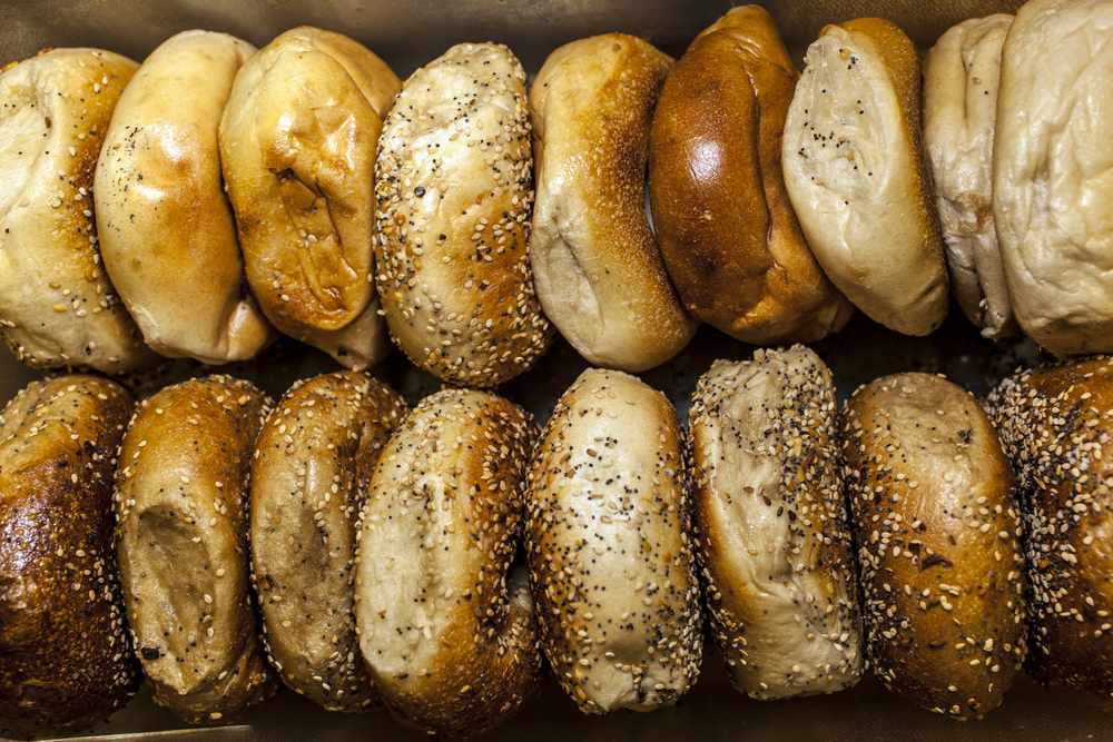 Fresh bagels, both plain and seeded, are arranged neatly in rows at a local bakery counter.