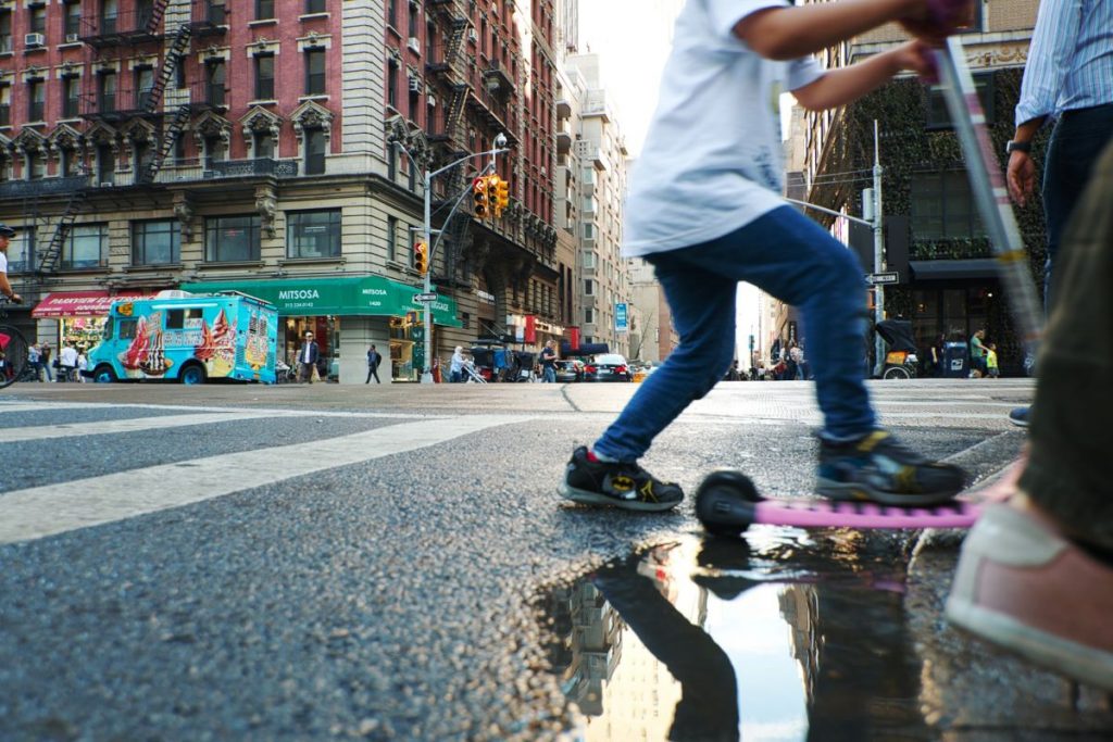 A boy on a scooter crossing the crosswalk in SoHo.