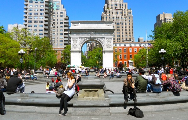 People gather around the fountain at Washington Square Park, relaxing beneath the Washington Square Arch with city buildings behind.