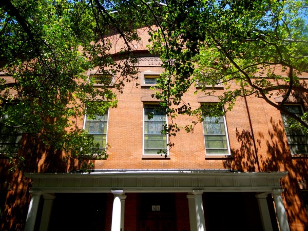 A red brick building in Brooklyn Heights with tall windows, white columns at the entrance, and leafy tree branches under clear skies.