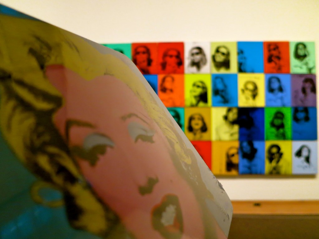 Marilyn Monroe’s face appears in bright pop art style by Andy Warhol, with similar colorful portraits arranged on a gallery wall.