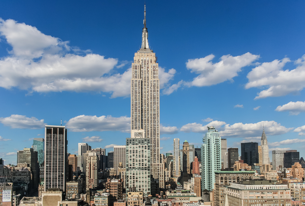 The Empire State Building towers above Manhattan’s skyline in New York City, surrounded by other skyscrapers under a clear blue sky.