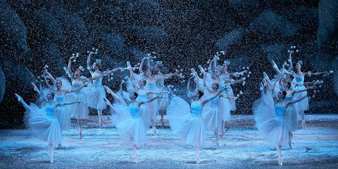 NYCB Nutcracker Ballet dancers in white tutus perform amid falling artificial snow on a New York stage, creating a magical, wintry scene.