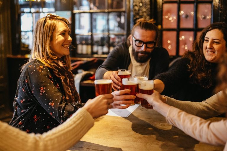 Four friends laugh and toast pints of beer in a cozy English pub, enjoying each other’s company and traditional pub camaraderie.