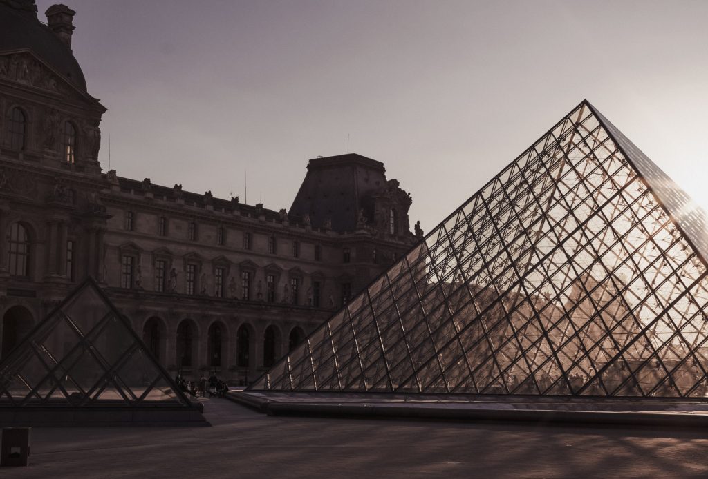 The Louvre Museum in Paris, featuring the large and small glass pyramids, at sunset, one of the best times to visit. 