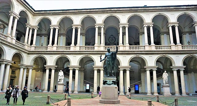 The courtyard at Pinacoteca di Brera in Milan displays a central statue of Napoleon by Antonio Canova, surrounded by visitors.