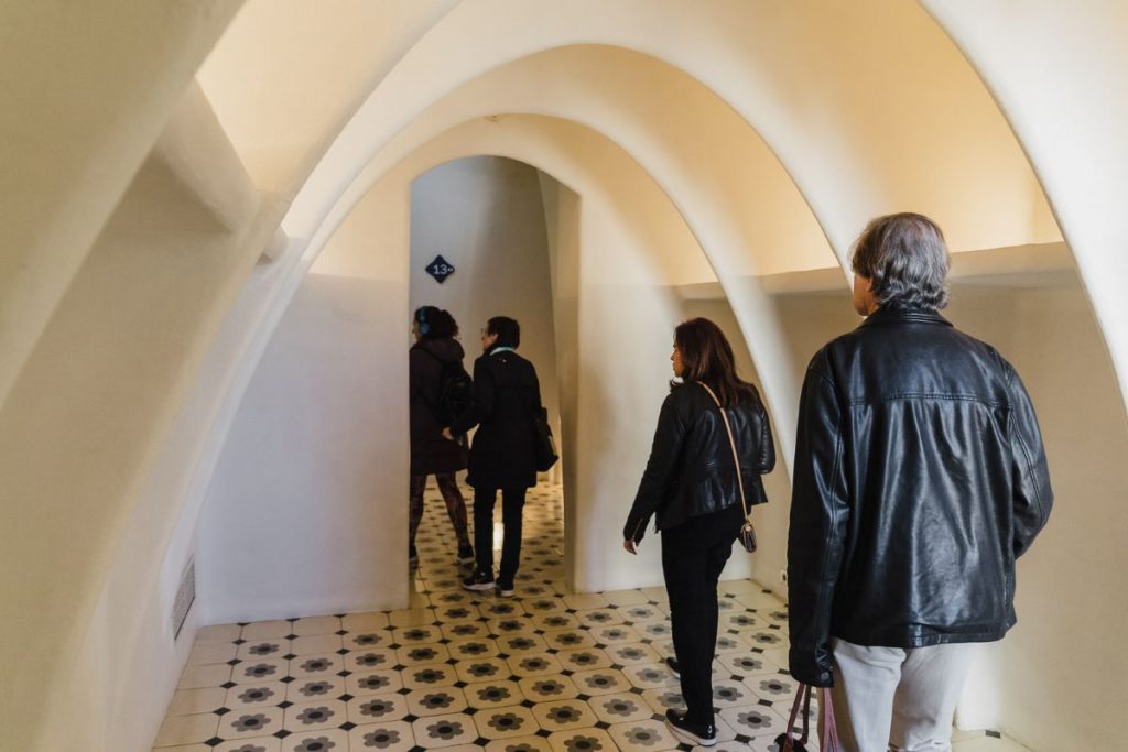 Guests walk through the arched hallways of Casa Batlló, crossing the beautifully decorated floral floor. One of the top Gaudi buildings Barcelona