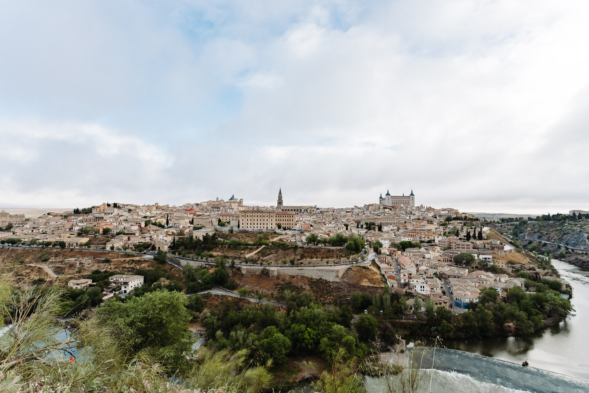 A sweeping view of Toledo, Spain shows the Alcázar fortress, historic buildings, and cathedral, all encircled by the Tagus River.