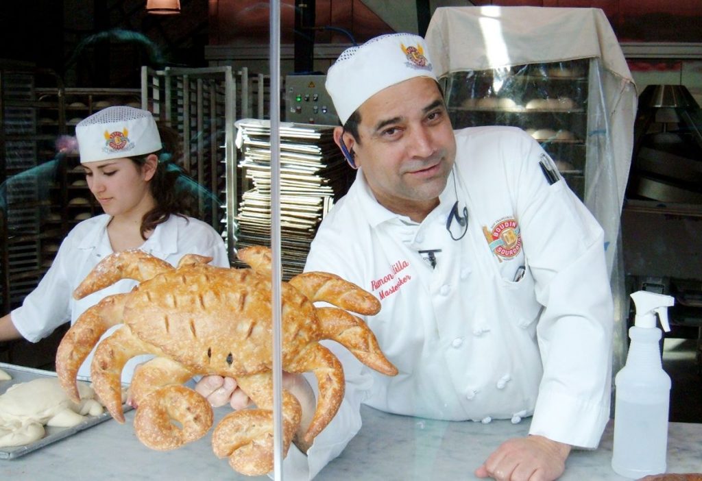 A worker at Boudin Bakery proudly displays a loaf of bread in the shape of a crab.
