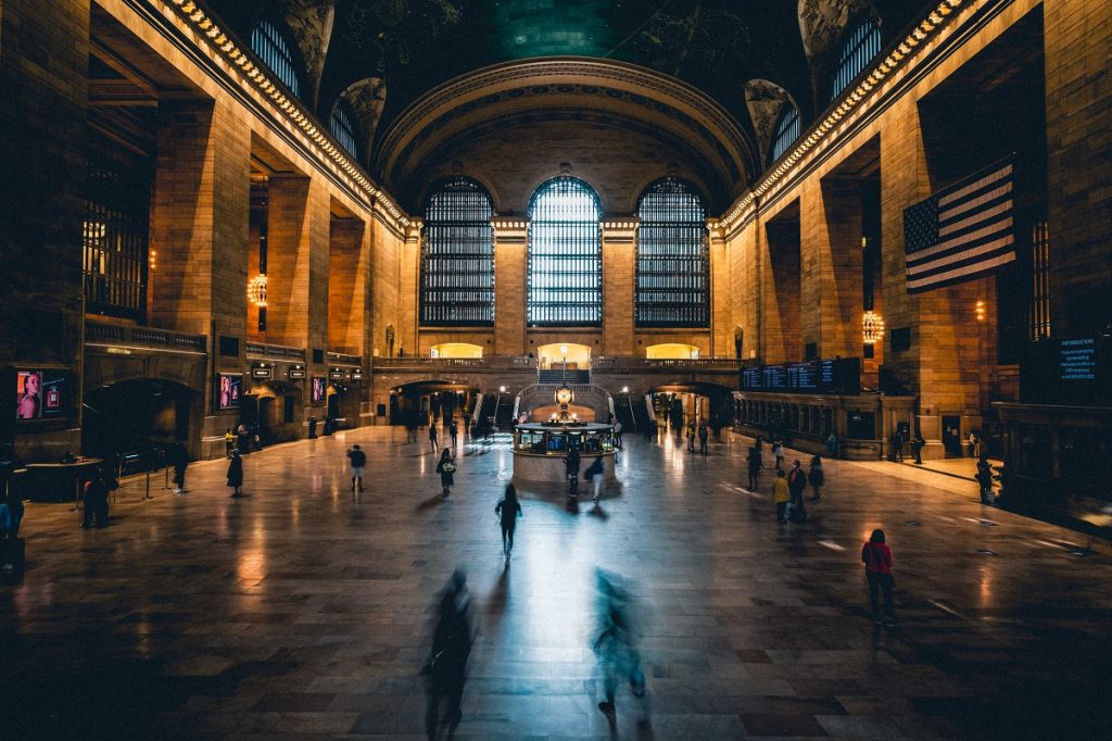 Grand Central Terminal’s main concourse glows under chandeliers, with travelers crossing marble floors beneath arched windows and the iconic clock.