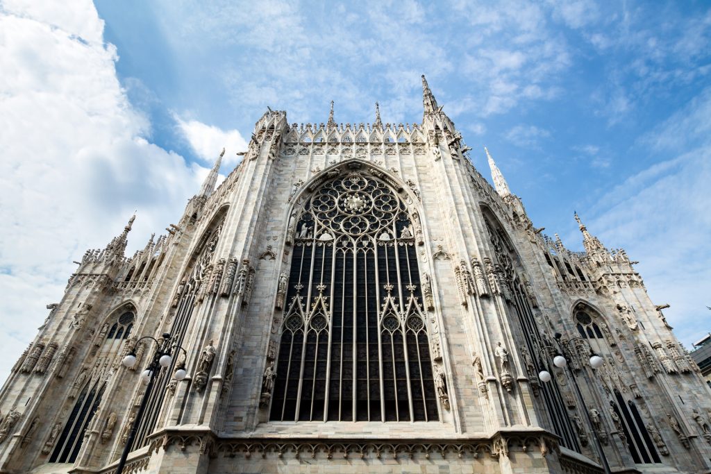 The ornate gothic facade of Milan’s Duomo features pointed arches, spires, intricate stonework, and a large rose window. It is a recommend stop for any self guided tour of Milan