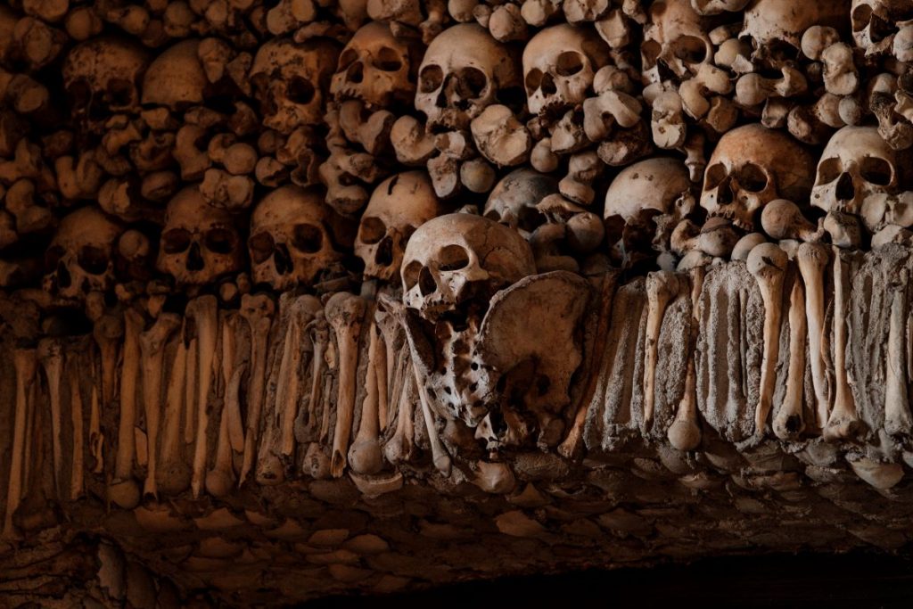 Human skulls and long bones are tightly stacked on a dimly lit wall in the Capela dos Ossos, one of the top things to do in Évora, Portugal.