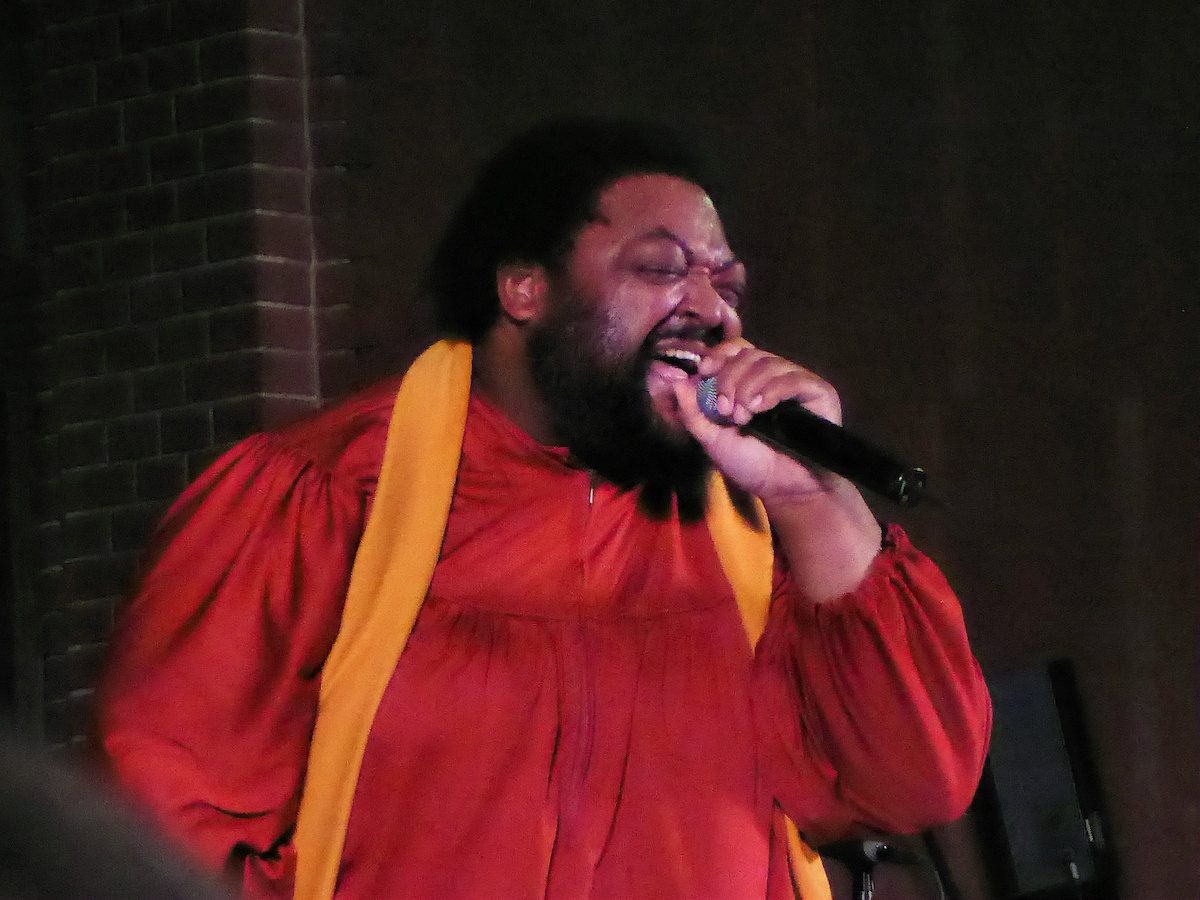 A Gospel singer in traditional brightly coloured robes, singing into a microphone