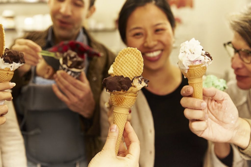 Four friends celebrate their multi day tour from rome, smiling and holding colorful ice cream cones with sprinkles and chocolate toppings. Warm atmosphere.
