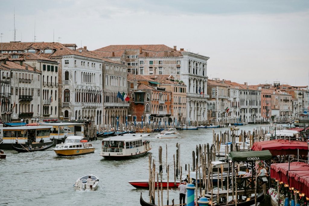 Boats and water taxis move along Venice’s Grand Canal, passing historic buildings as people dine at waterside cafes.