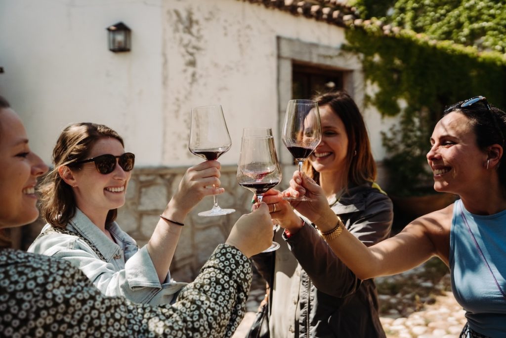 Four women holding glasses of red wine and cheering.