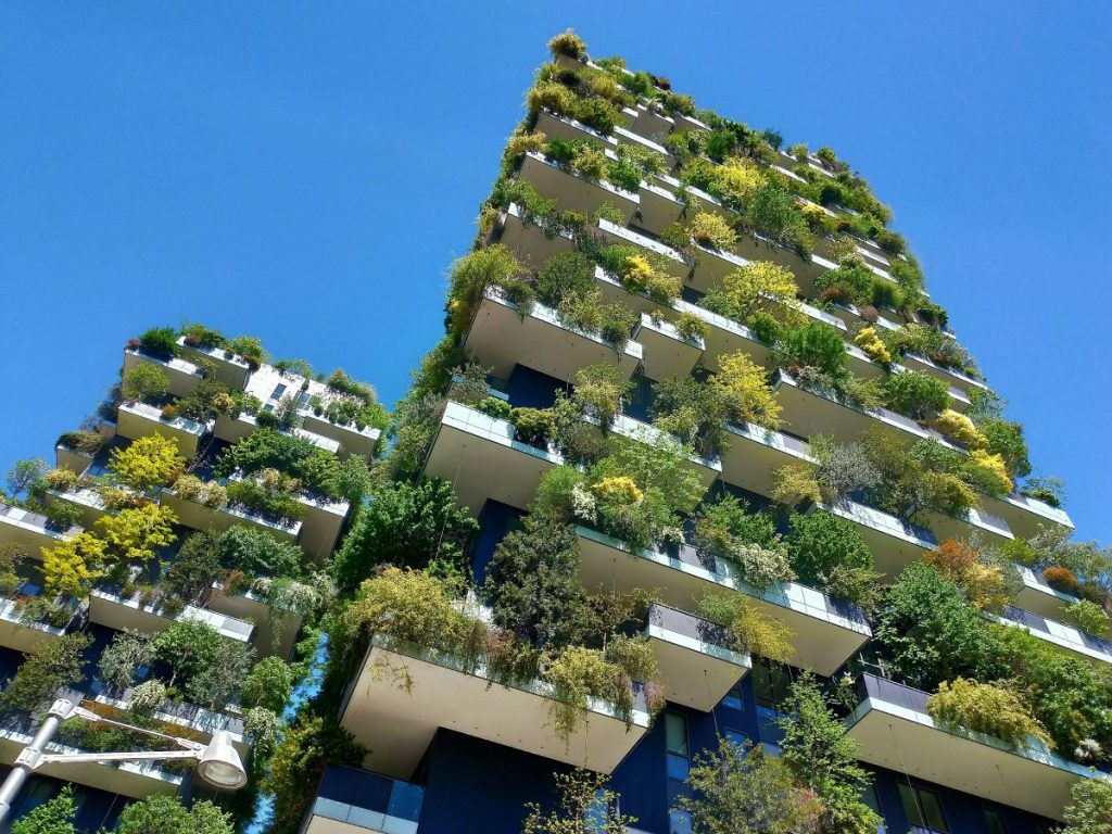 A pair of high rise apartment blocks, with greenery and hanging plants from each balcony, against a bright blue sky. An example of the modern architecture in Milan