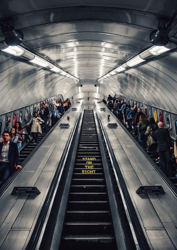 People using public transportation. In the middle escalator words that say "stand on the right" can be read.