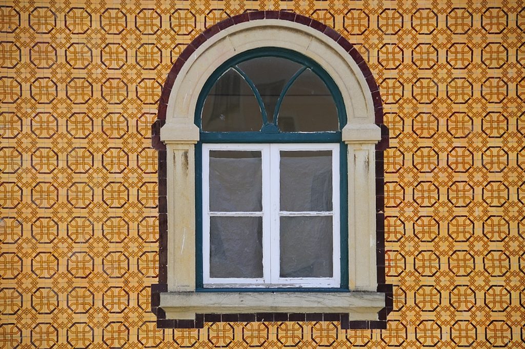 A green-framed arched window shows curved upper panes and four rectangular lower panes, set in a beige wall with orange geometric wallpaper.