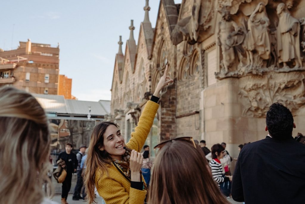 A woman in a yellow coat leads a tour group outside Barcelona’s historic carved stone building, pointing out notable literary landmarks.