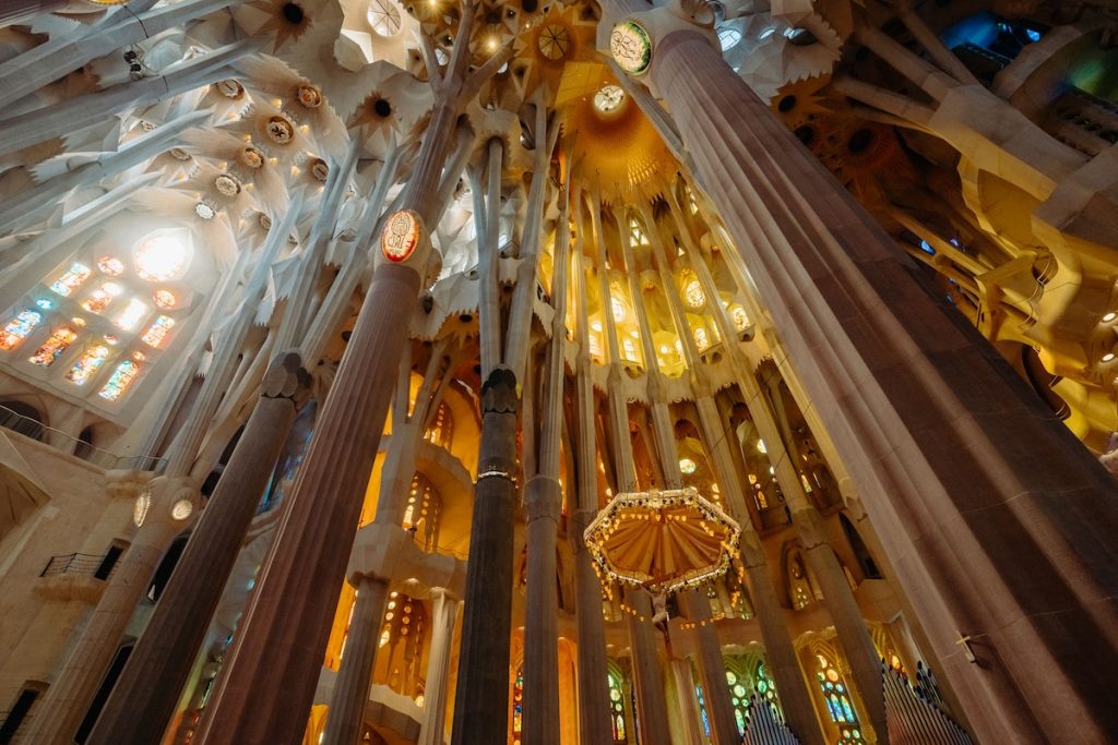 A cathedral nave with towering stone columns and stained glass windows casts colorful light, creating a warm, vibrant atmosphere inside.