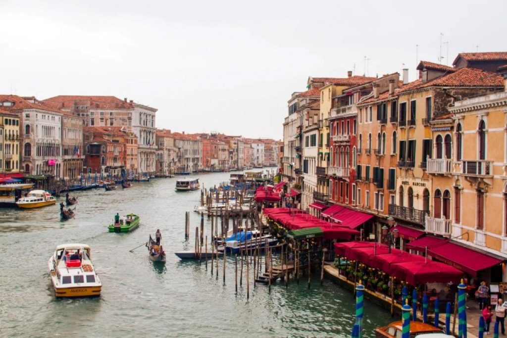 Different types of boats in a large canal in Venice with buildings on either side.