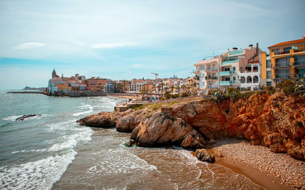 a beach town near barcelona - a deserted beach, surrounded by rocks with a bay and coastal buildings during daytime