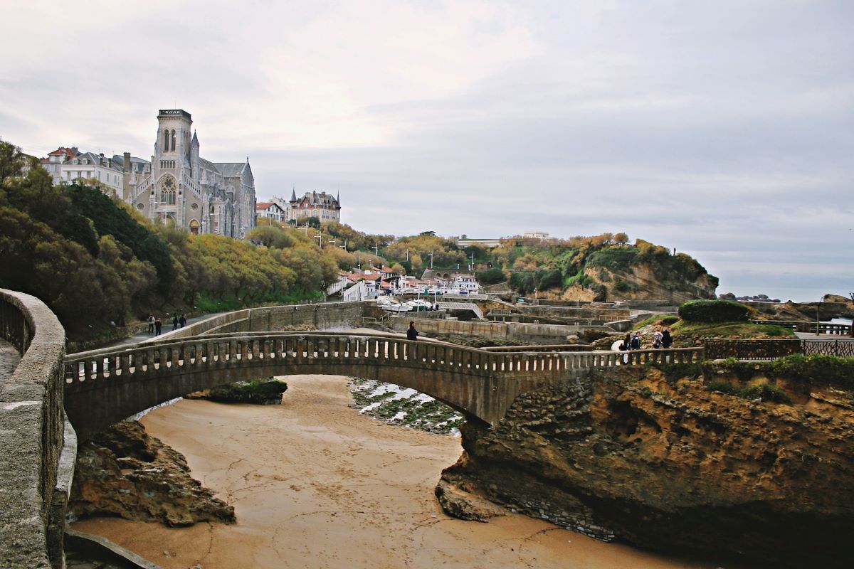 People walking over a bridge going over the beach in Biarritz.