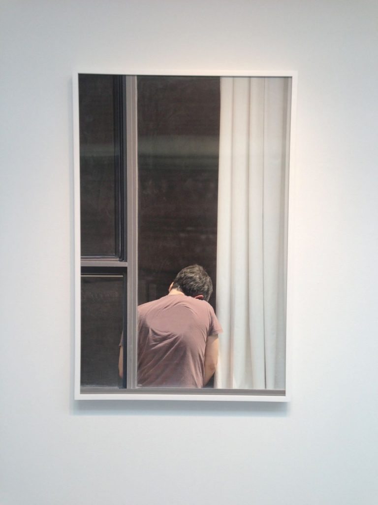 A photo of a picture in one of the Boston art galleries, which depicts a window with a man inside, with his back pressed against the window.