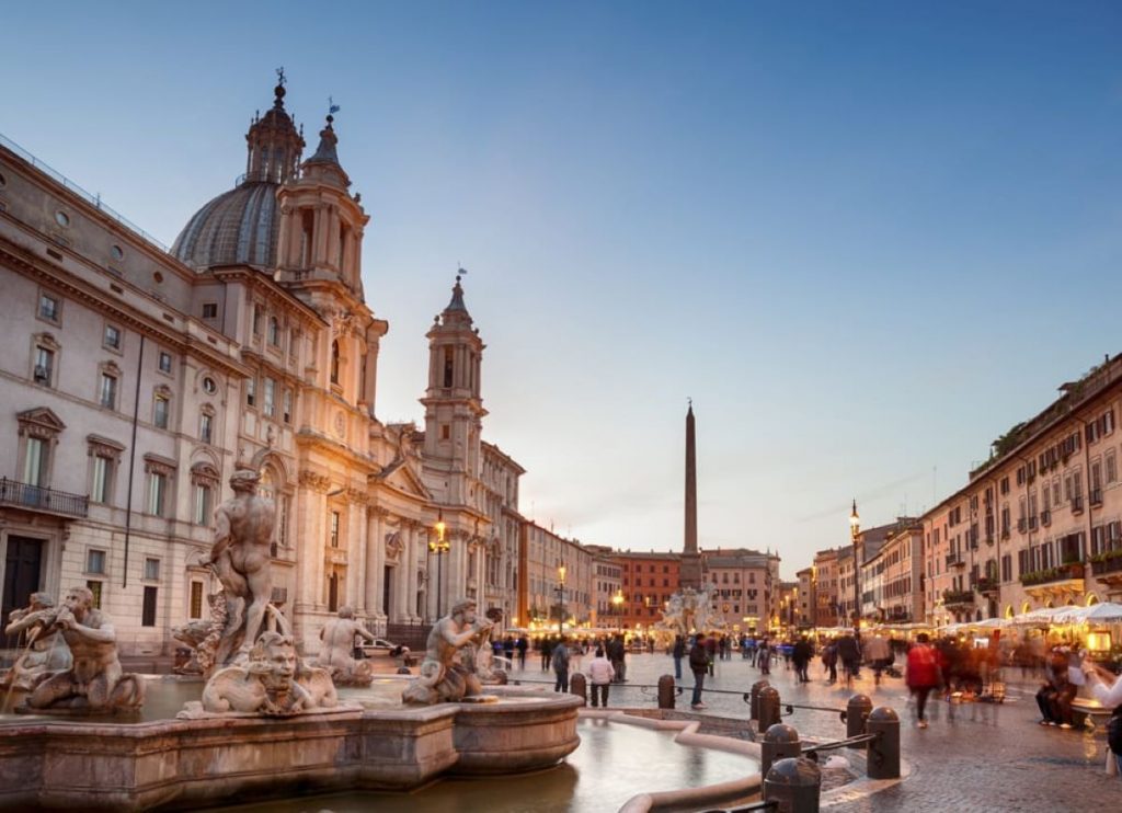 Crowds gather near illuminated cafes and Bernini’s Fountain of the Four Rivers by Sant’Agnese in Agone church, Piazza Navona, Rome.