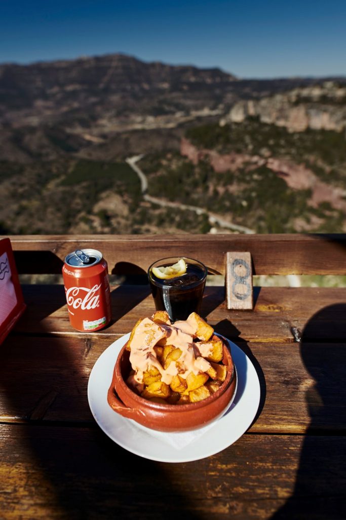 Patas bravas next to a glass of coke with mountains in the background.