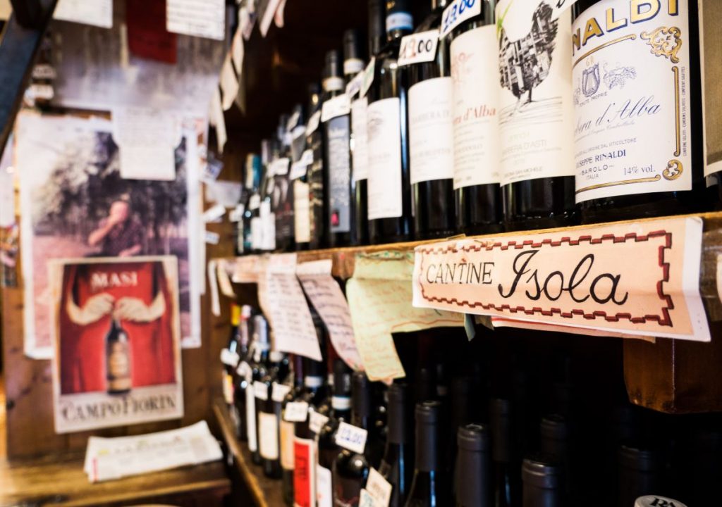 Several wine bottles line wooden shelves at Cantine Isola in Milan, with handwritten signs and a vintage Masi Campofiorin poster.