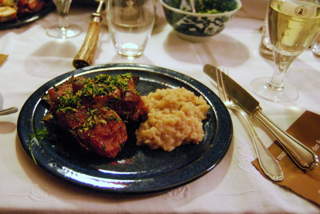 a plate of MIlanese food on a table in a restaurant, including ossobuco, which is a veal shank, and a side serving of creamy risotto.