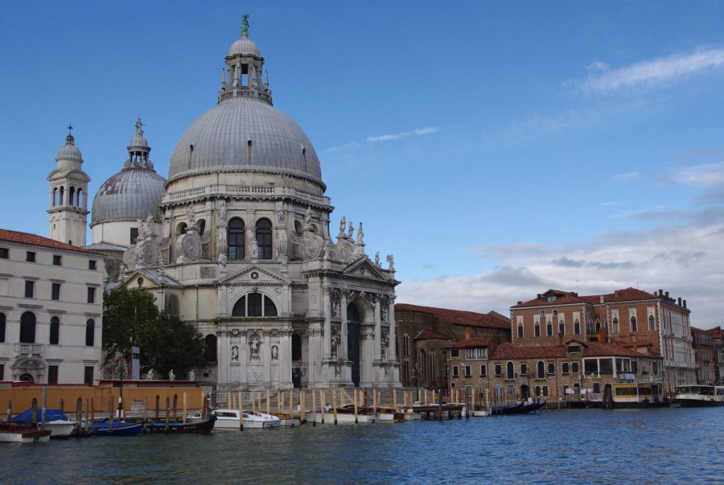 Santa Maria della Salute’s grand dome rises beside Venice’s Grand Canal, with colorful boats and historic buildings along the waterfront.