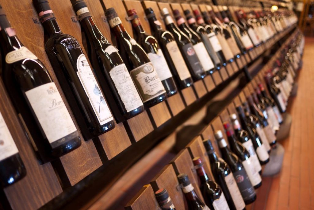 Several wine bottles rest angled downward on wooden shelves in a Milan store, evoking the city’s stylish wine bar atmosphere.