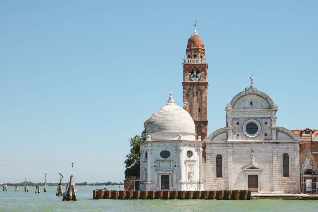 A small white brick Roman Catholic church with dome, ornate facade and bell tower on one of the Venetian Islands - San Michele.