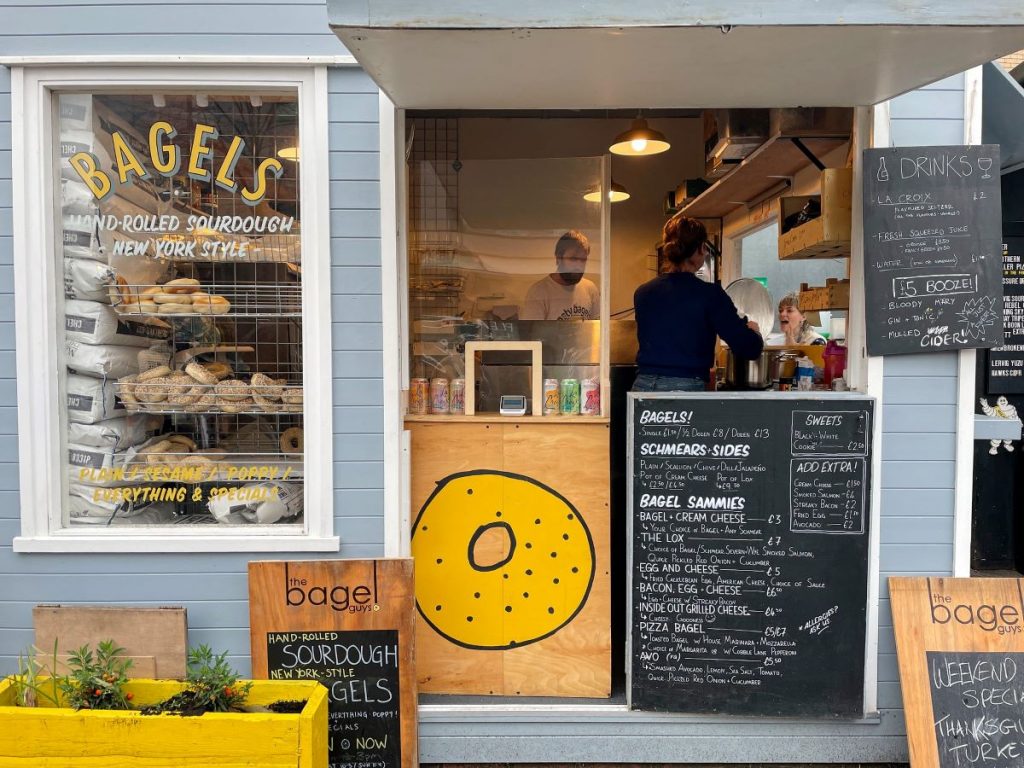 Storefront of The Bagel Guys, one of the best bagels in London, while workers help customers inside.