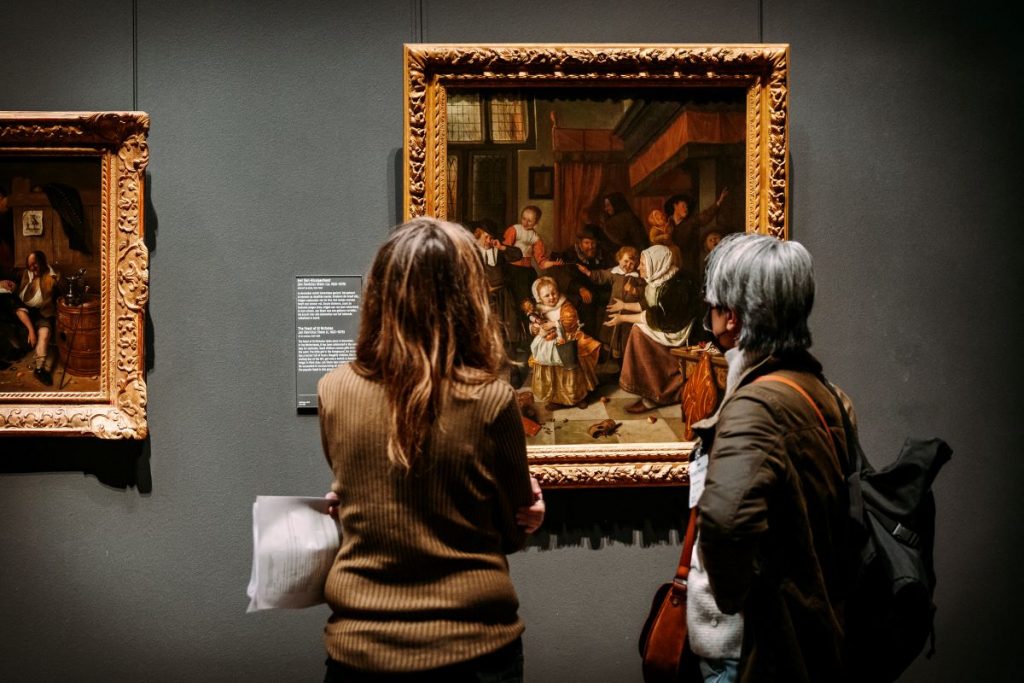 Painting of Jan Steen, Feast of St Nicholas, while to people look at the painting.
