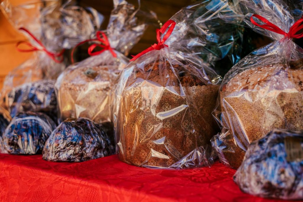 Round loaves of panettone bread wrapped in clear plastic with red ribbons rest on a red tablecloth at a Venice Christmas market. The ideal gift idea for travel lovers. 