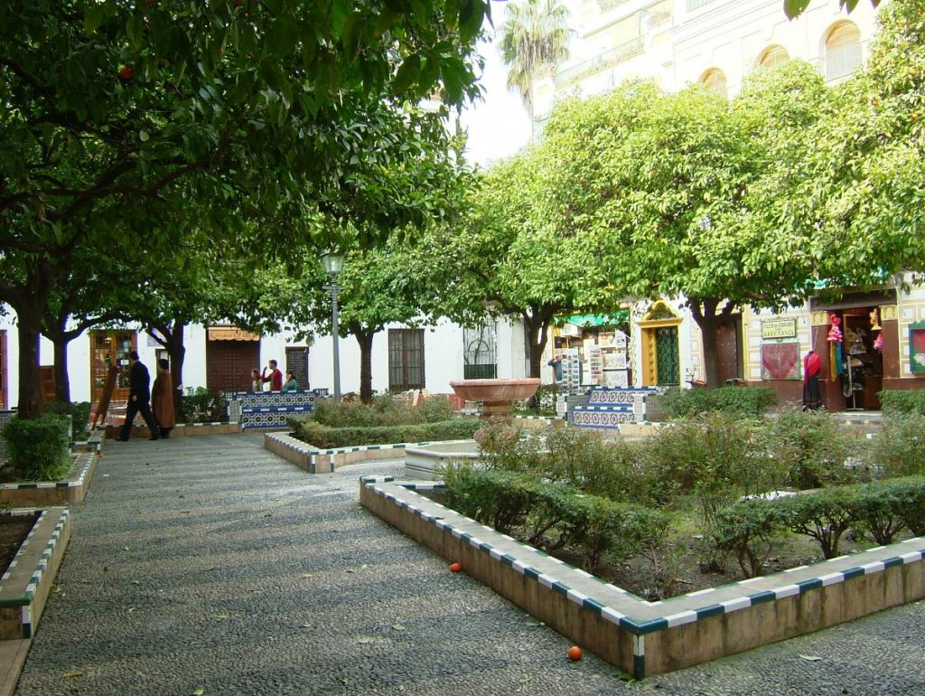 a beautiful small spanish plaza in seville, with pathways and gardens, a central fountain and tiled benches. one of the famous opera spots in seville