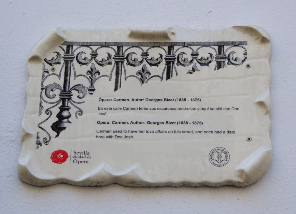 A commemorative white ceramic plaque for the opera carmen, fixed on a white wall. these plaques are all around seville to show the famous opera spots
