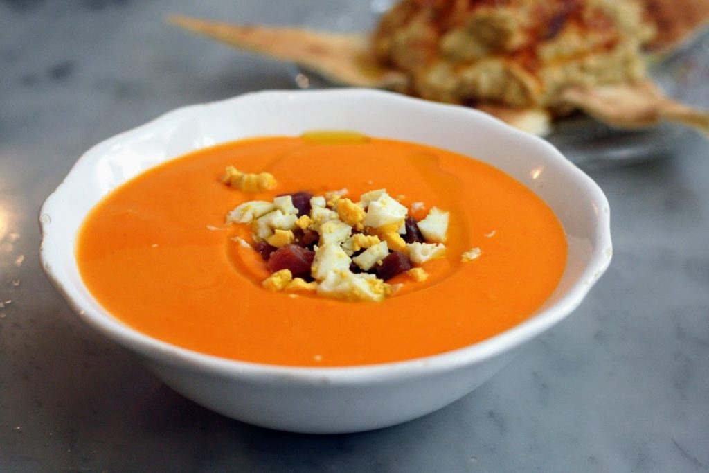 A bowl of salmorejo, a creamy orange Spanish soup, is topped with chopped egg and ham, in a Madrid tavern.