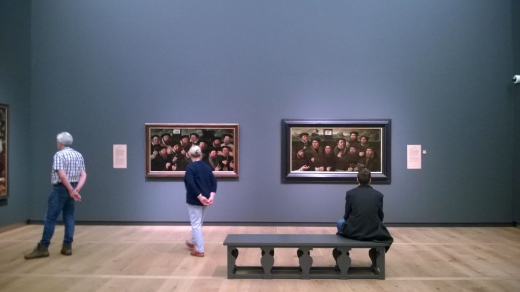 A man sitting on a bench looking at paintings at the H'ART museum in Amsterdam.