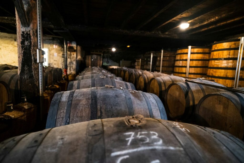 Rows of wooden barrels for aging sherry are stacked in a dim cellar in Jerez, Spain, with rustic dark walls.