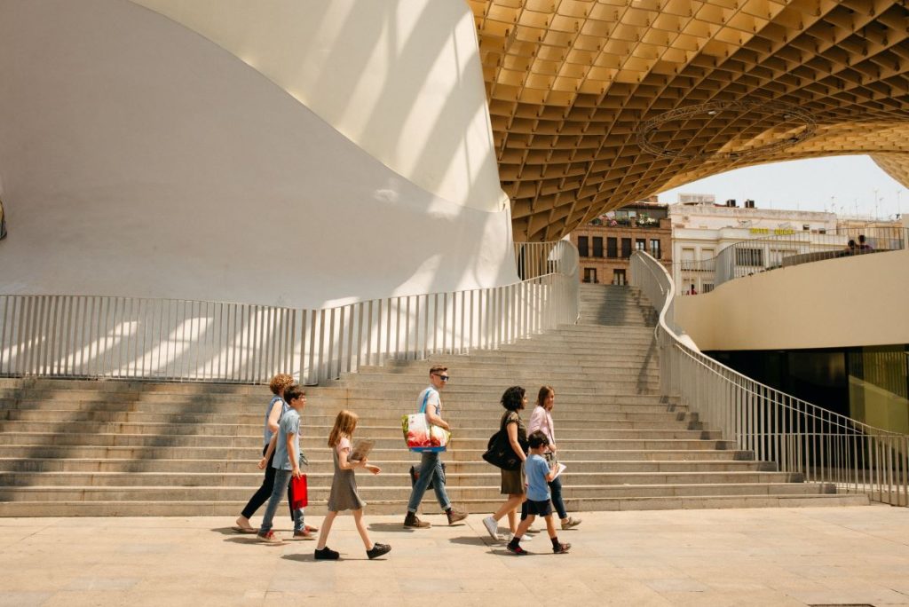 Six people, including adults and children, walk past Metropol Parasol’s curved white walls and yellow lattice canopy in Seville, Spain.