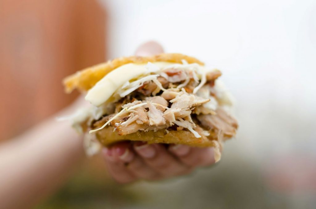 A person holding an arepa filled with meat and cheese.