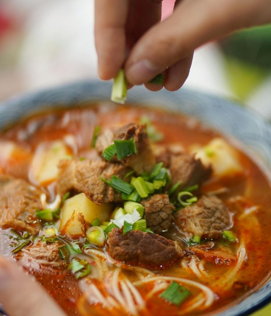 A person sprinkling green onions in their Thai noodle soup at a restaurant in Astoria, Queens.