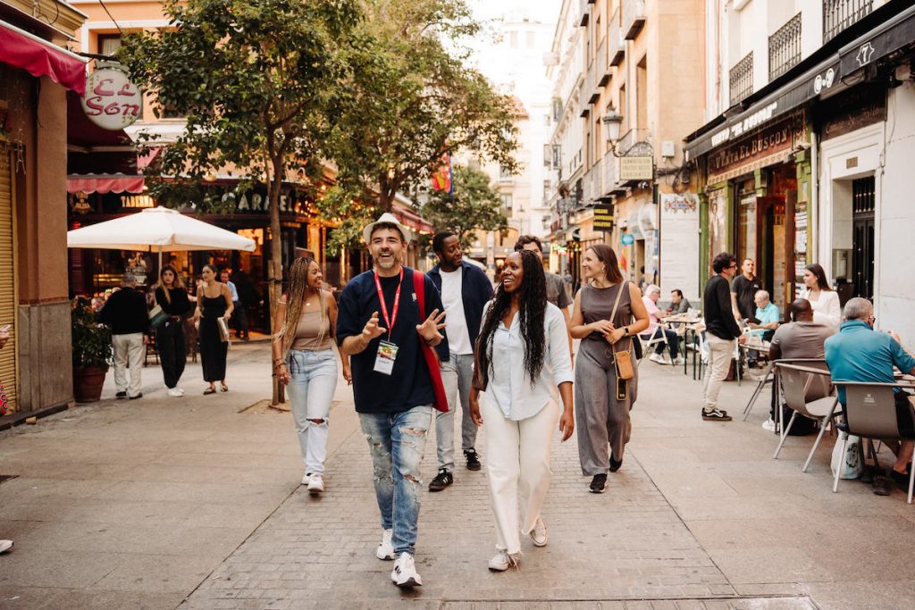 People walk around Madrid's center passing shops and cafes as others relax at outdoor tables. The city is easy to navigate when solo traveling in Madrid