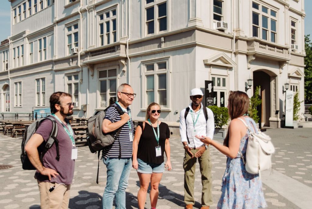 Five adults stand at Battery Park in London, smiling and talking as one person leads a guided tour.